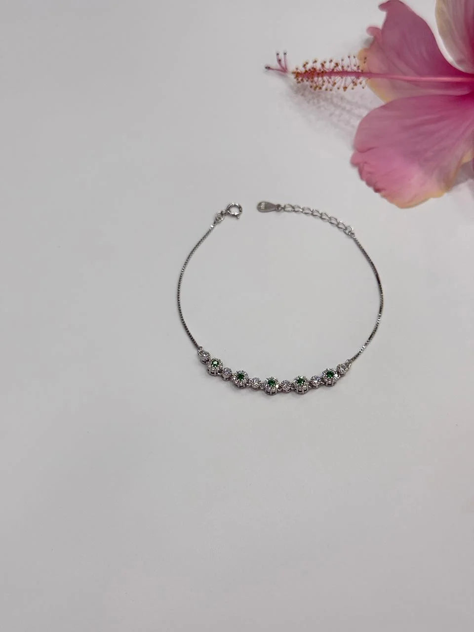 Silver bracelet with small stones on a light gray background with a pink flower.