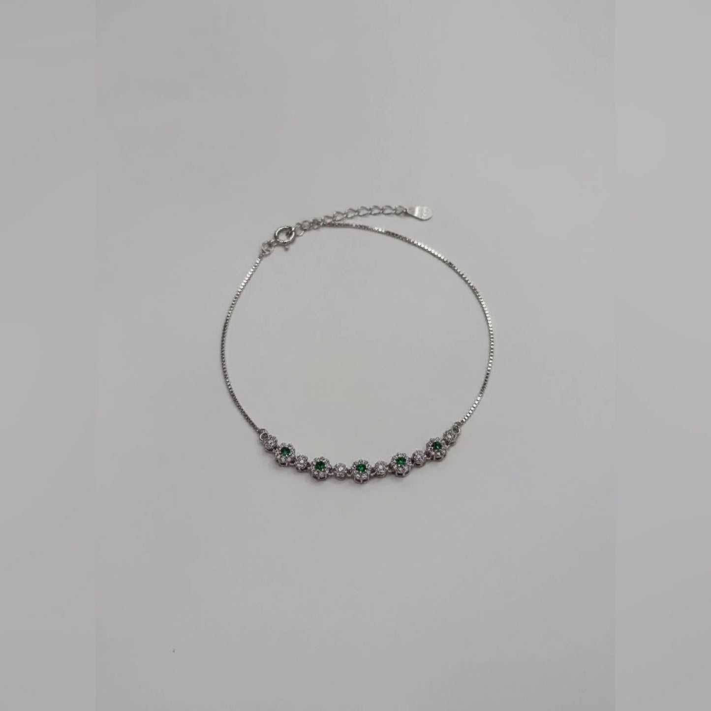 Silver bracelet with green and purple stones on a light gray background