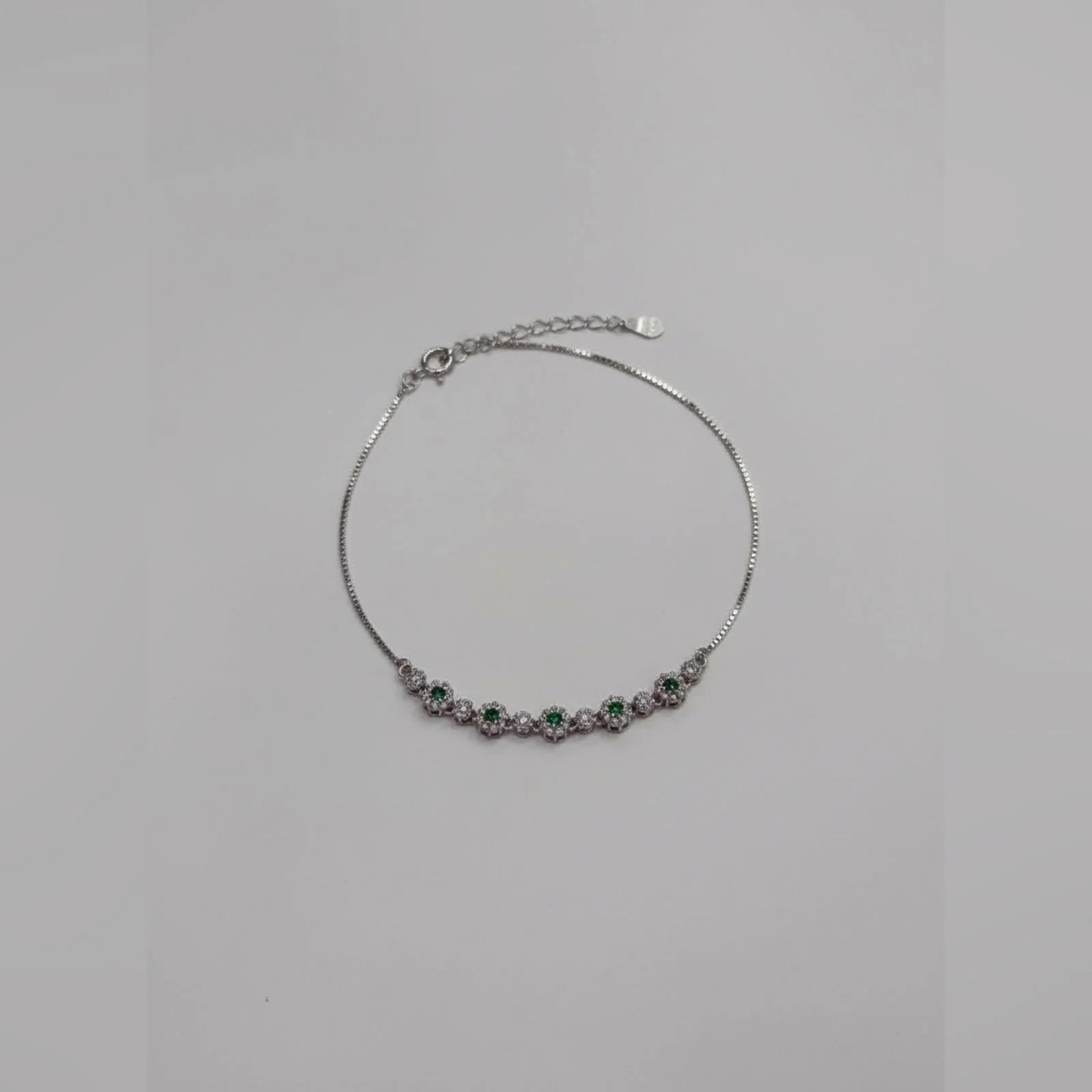 Silver bracelet with green and purple stones on a light gray background