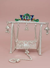 Decorative silver swing with peacock top on a pink background