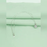 Silver necklace with a heart-shaped pendant on a light green background