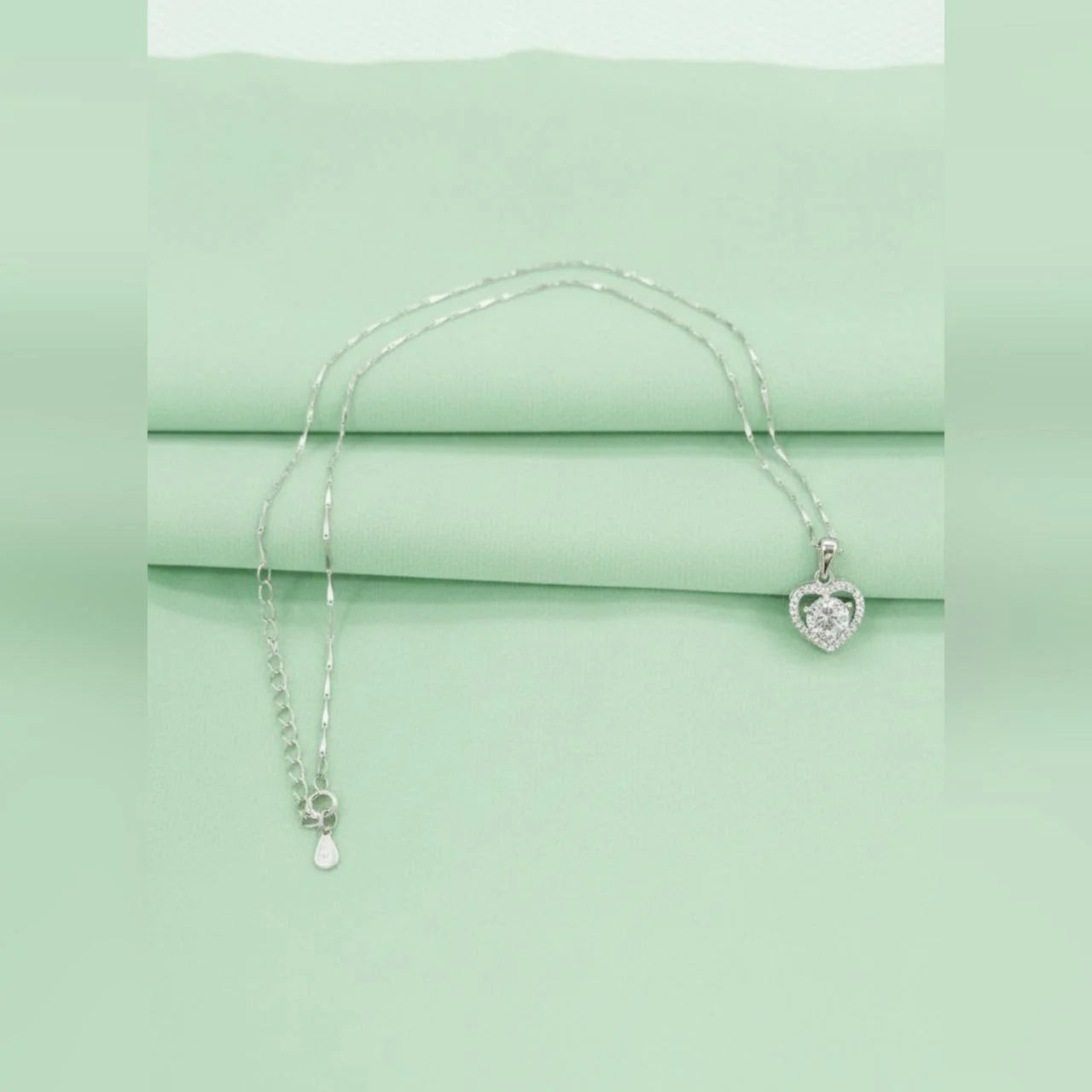 Silver necklace with a heart-shaped pendant on a light green background