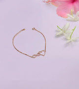 Rose gold bracelet with heart and infinity symbol on a light purple background with flowers.