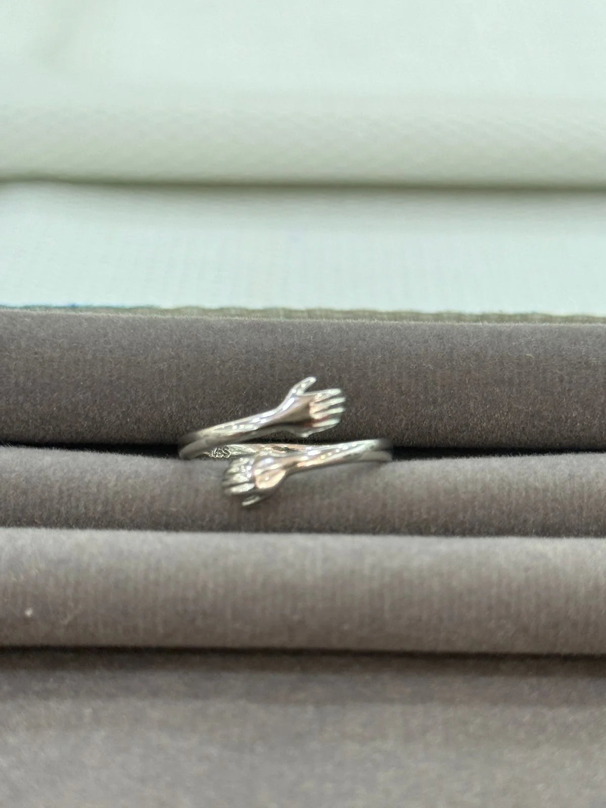 Silver ring with hug design on a textured surface