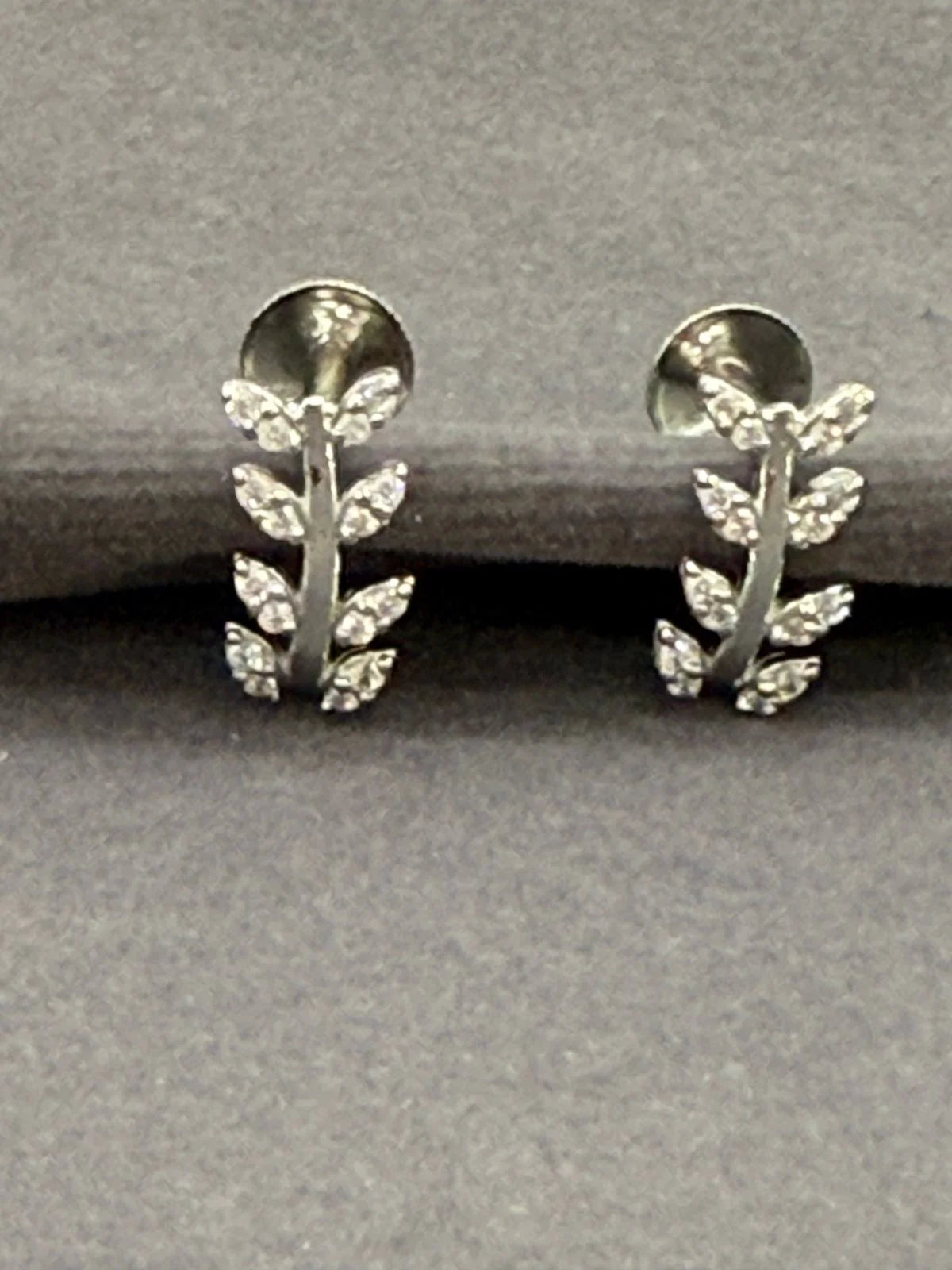Silver leaf-shaped earrings on a gray background