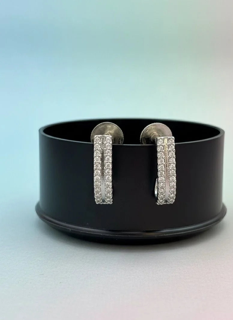 Pair of silver hoop earrings on a black stand with a gradient background