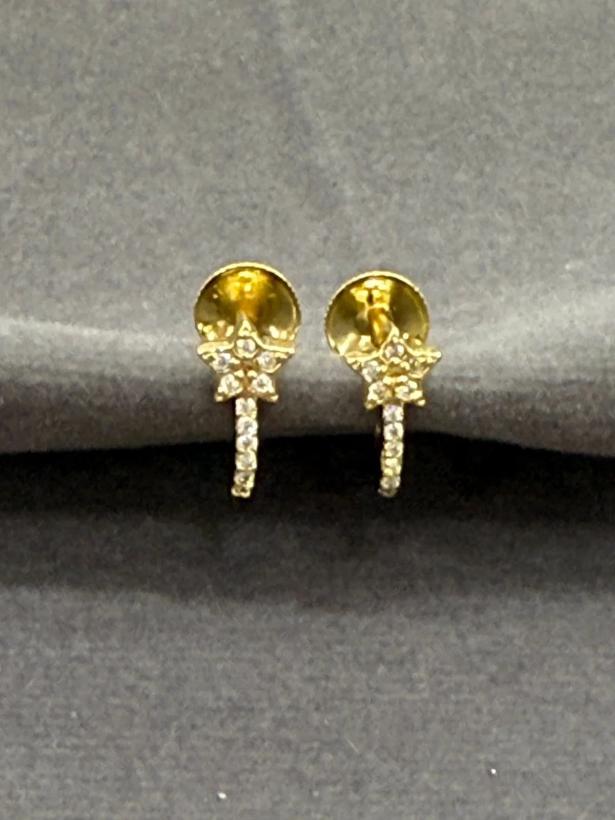 Gold earrings with gemstones on a gray surface