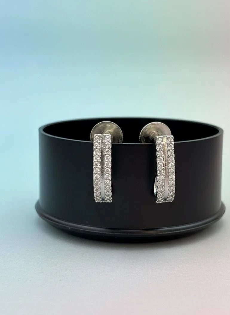 Pair of silver hoop earrings on a black stand with a gradient background