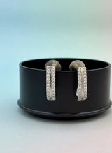 Pair of silver hoop earrings on a black stand with a gradient background