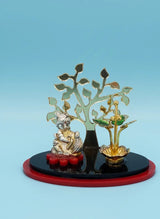 Decorative item with a statue, tree, and bowl on a black base against a blue background