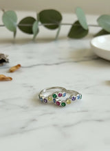 Silver toe ring with colorful gemstones on a marble surface with eucalyptus leaves.