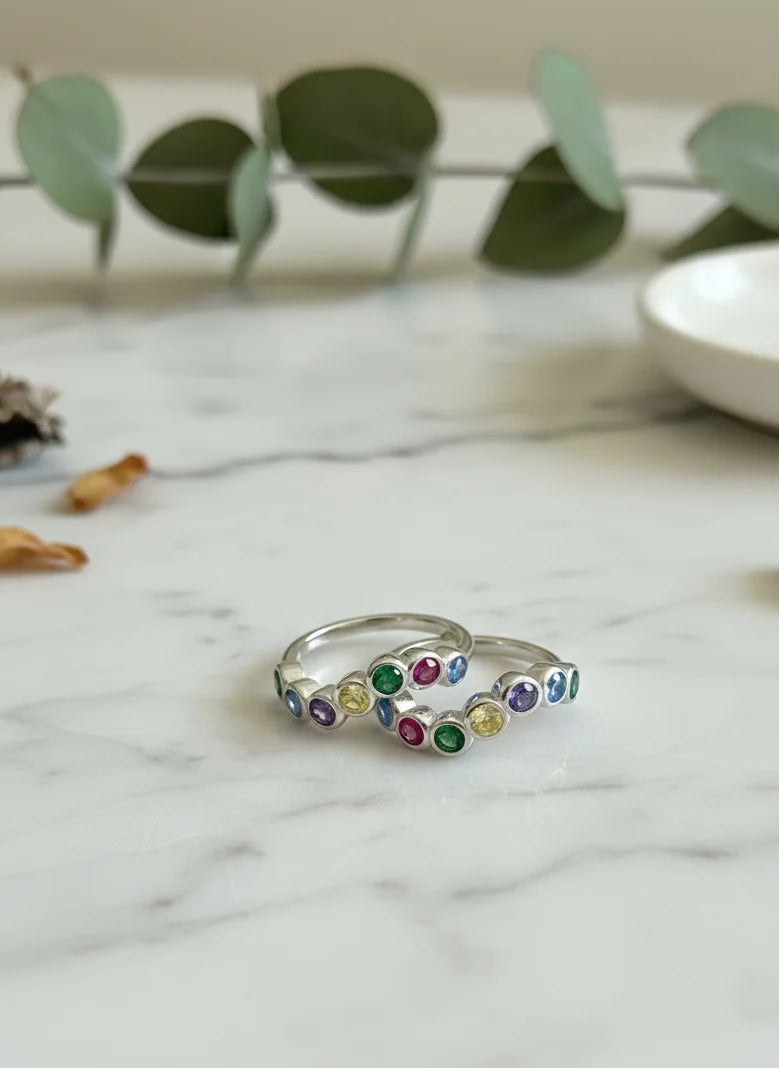 Silver toe ring with colorful gemstones on a marble surface with eucalyptus leaves.