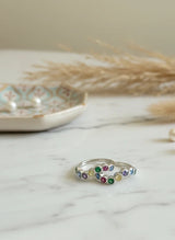 Silver toe ring with colorful gemstones on a marble surface with pearls and dried plants.