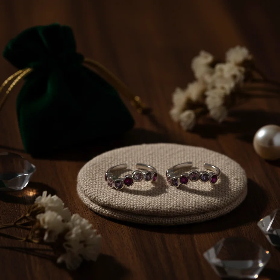 Two toe rings with gemstones on a textured surface with decorative elements.