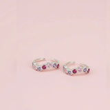 Silver toe rings with colorful gemstones on a pink background