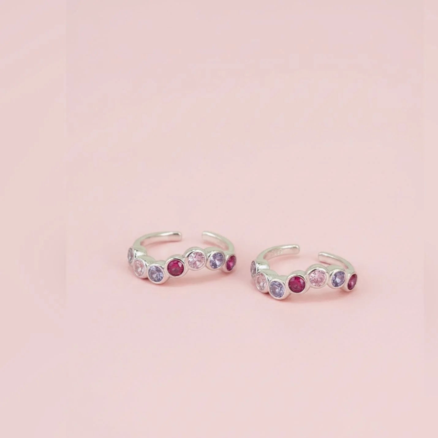 Silver toe rings with colorful gemstones on a pink background