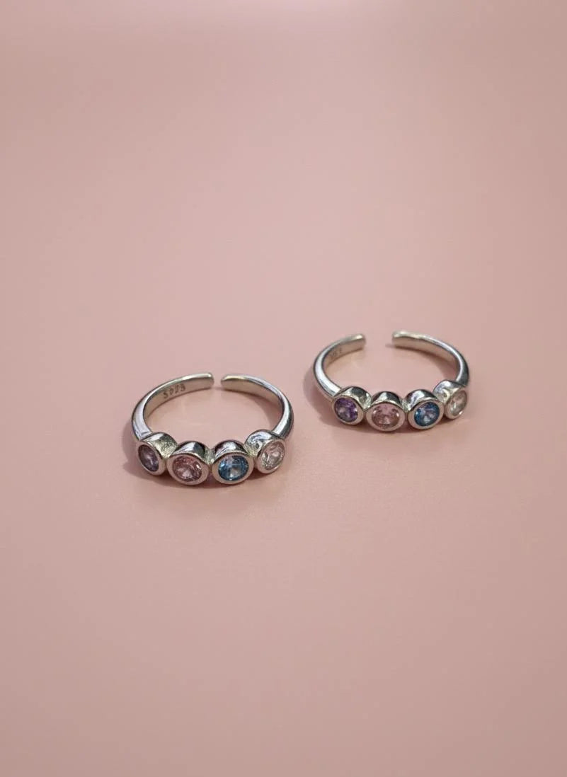 Two toe rings with colorful gemstones on a pink background