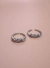 Two toe rings with colorful gemstones on a pink background