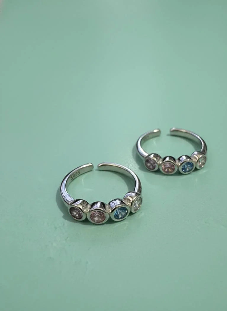 Pair of silver toe earrings with colorful gemstones on a light green background