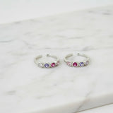 Two silver toe rings with colorful gemstones on a marble surface