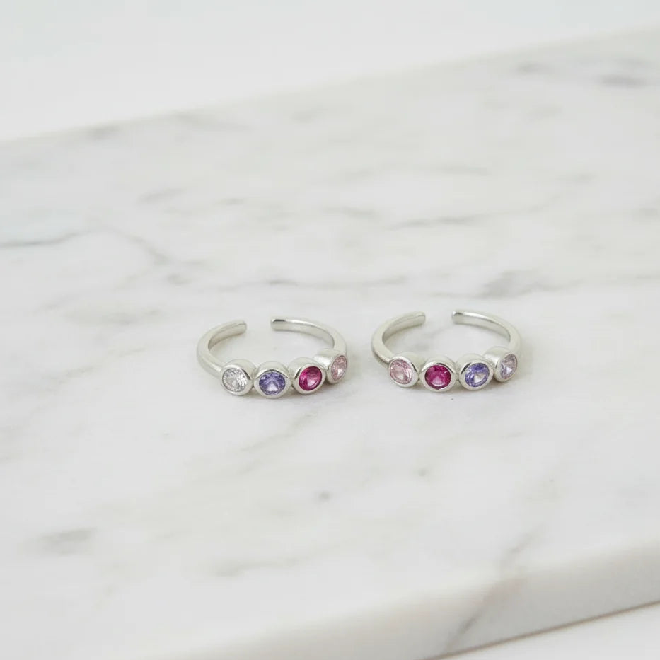 Two silver toe rings with colorful gemstones on a marble surface