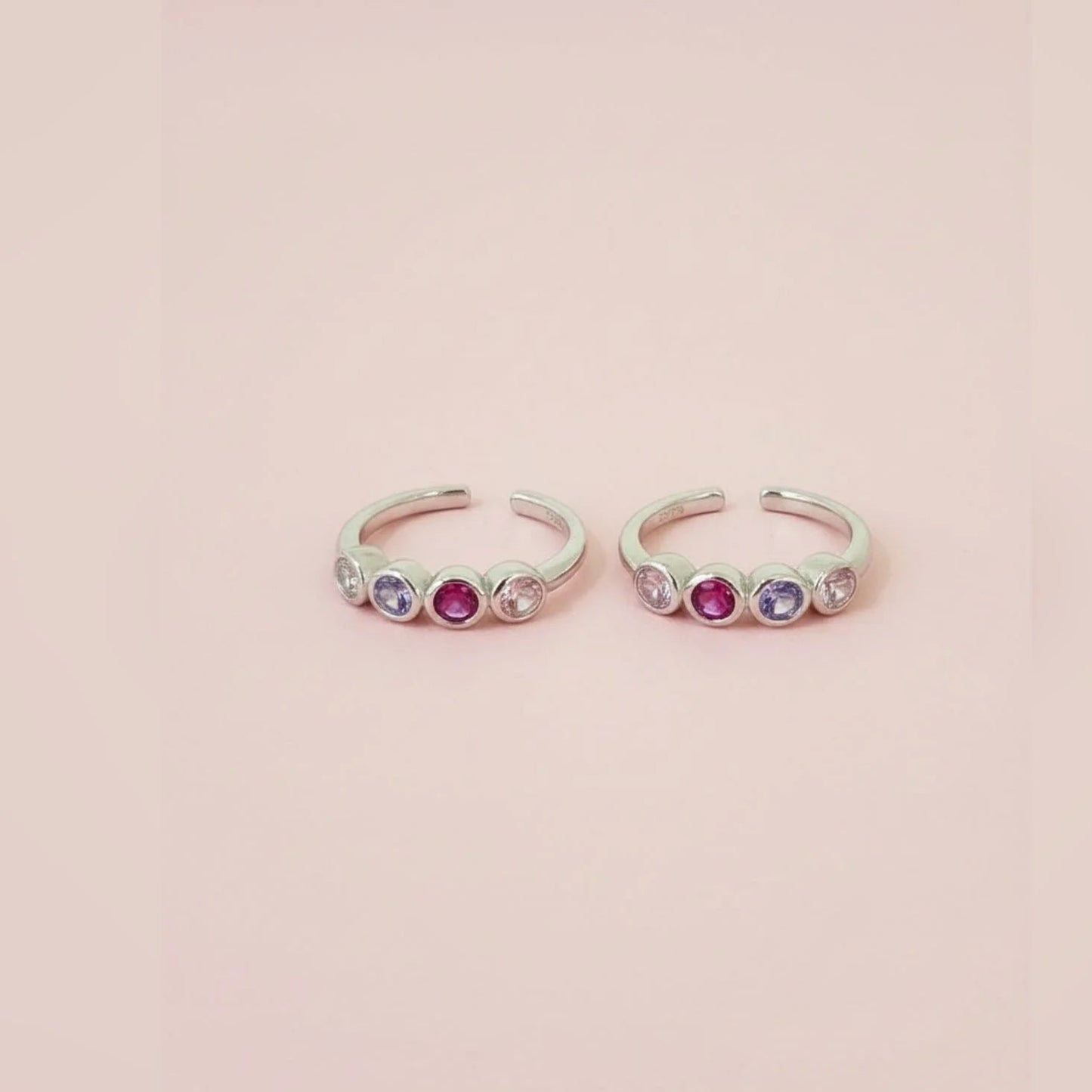 Two silver toe  rings with colorful gemstones on a pink background