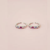 Two silver toe  rings with colorful gemstones on a pink background