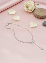 Silver necklace with a leaf pendant on a pink surface with flowers and stones.