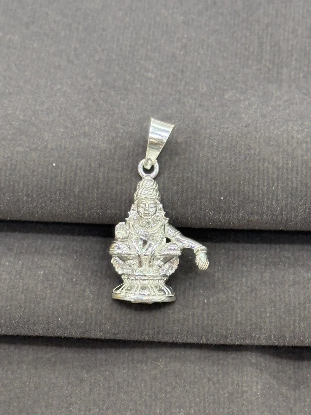 Silver pendant with a deity figure on a gray surface