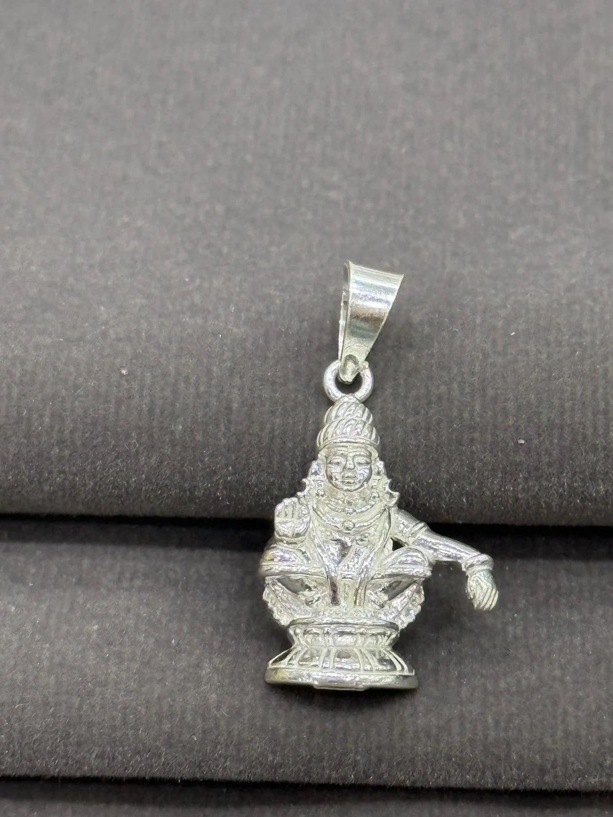 Silver pendant with a deity figure on a gray background