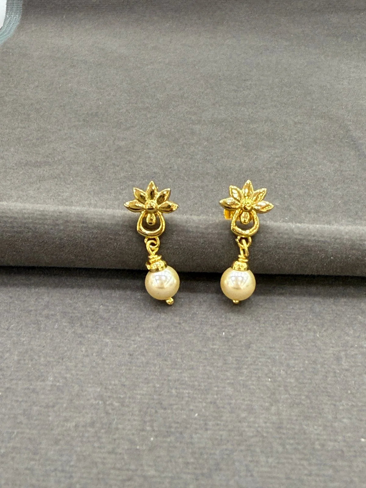 Gold earrings with pearl drops on a gray surface