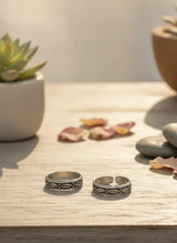 Two silver toe rings on a wooden surface with decorative elements.