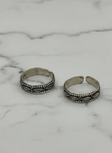 Two silver toe rings with intricate designs on a marble surface