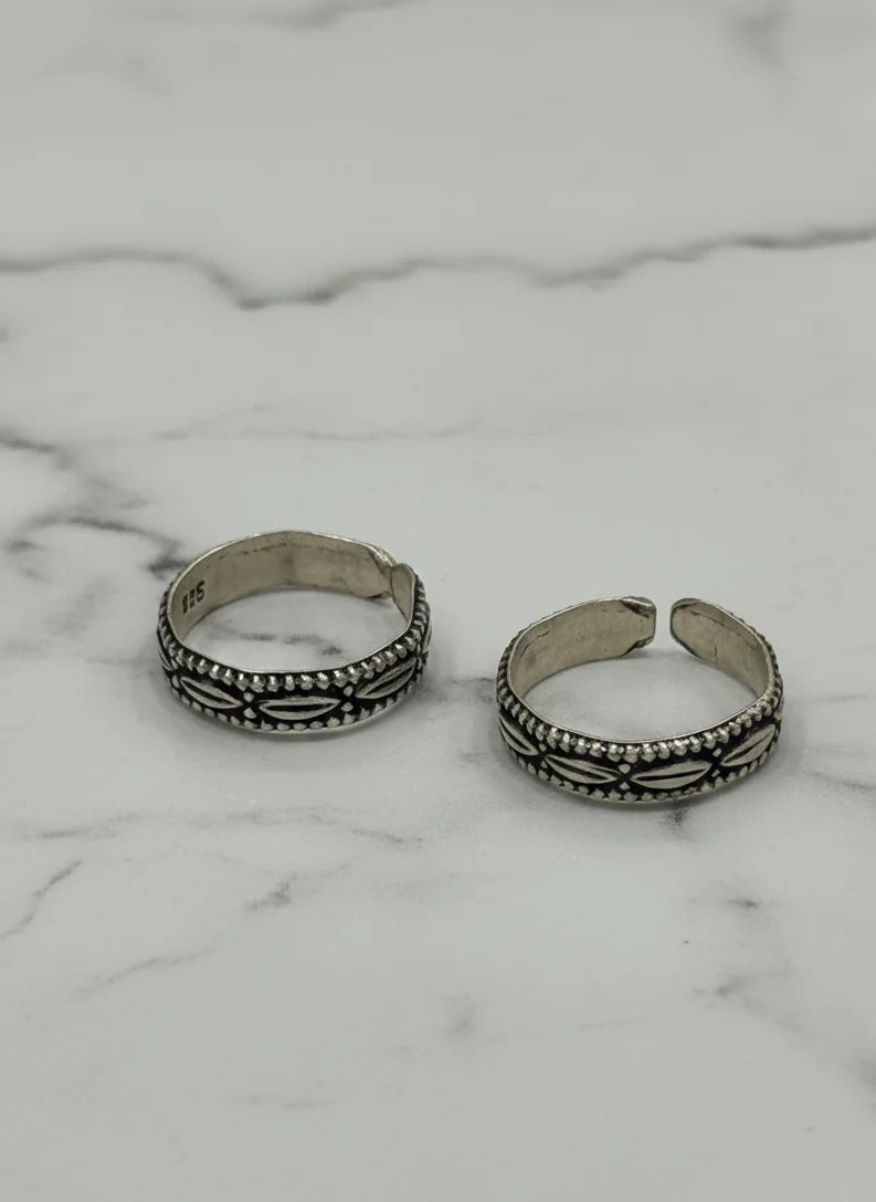 Two silver toe rings with intricate designs on a marble surface