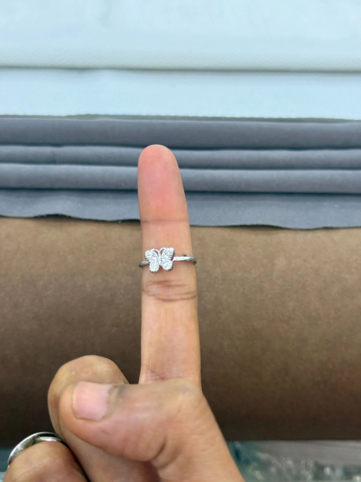 Silver butterfly ring on a finger against a neutral background
