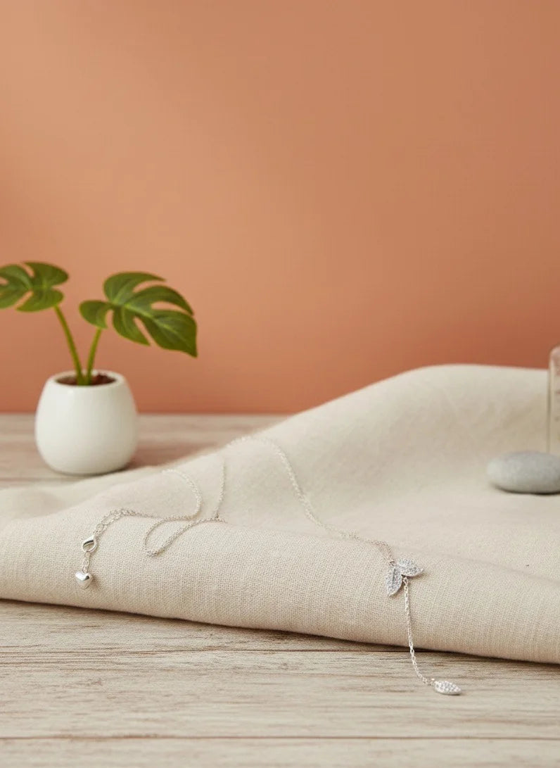 Necklaces on a beige fabric with a plant and bottle in the background