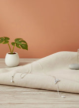 Necklaces on a beige fabric with a plant and bottle in the background