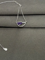 Silver necklace with a purple gemstone on a gray surface