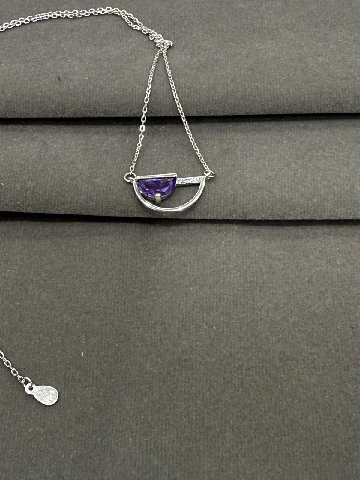 Silver necklace with a purple gemstone on a gray surface