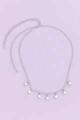 Silver necklace with small round pendants on a light purple background