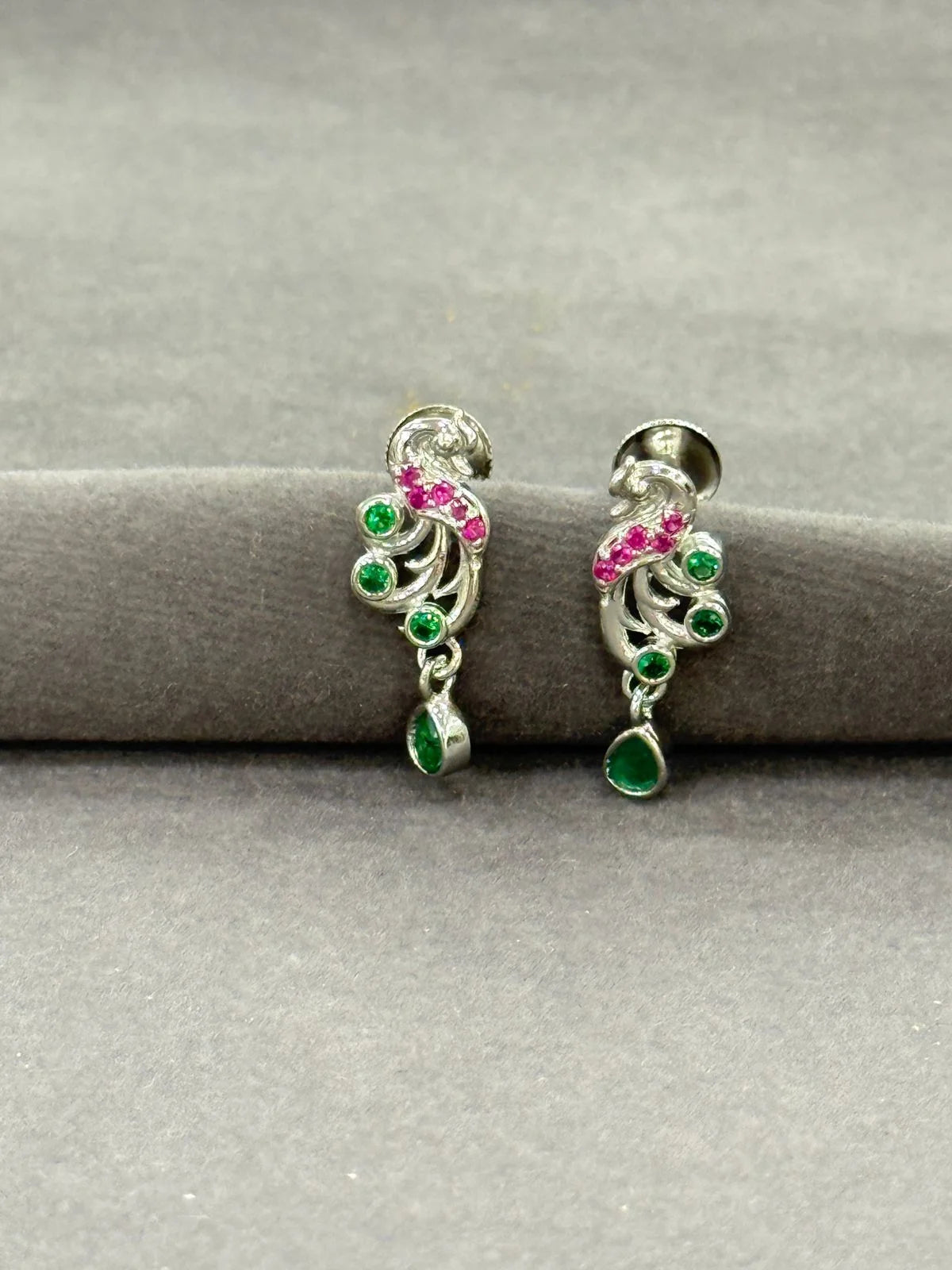 Pair of silver earrings with green and pink gemstones on a gray surface