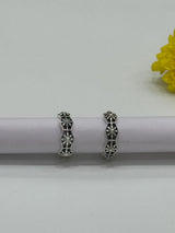 Silver toe earrings on a white surface with a yellow flower in the background