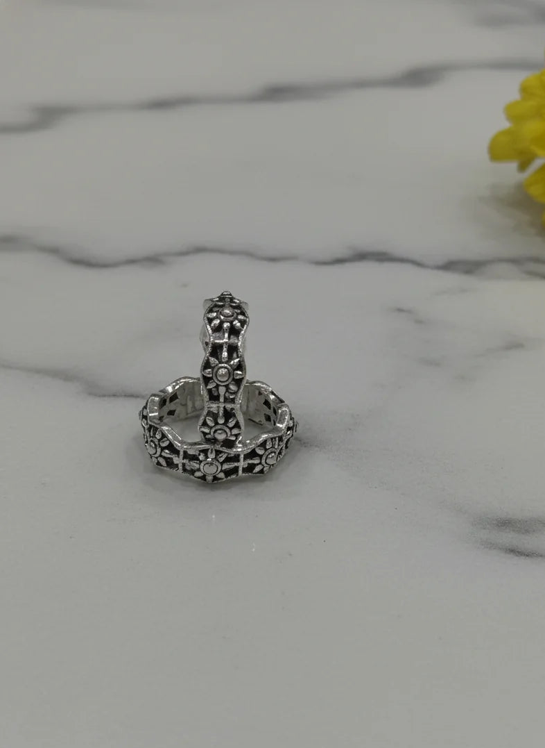 Silver toe ring with intricate design on a marble surface with a yellow flower.