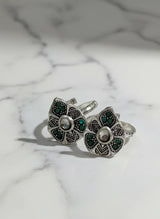 Pair of silver floral toe rings with green gemstones on a marble background