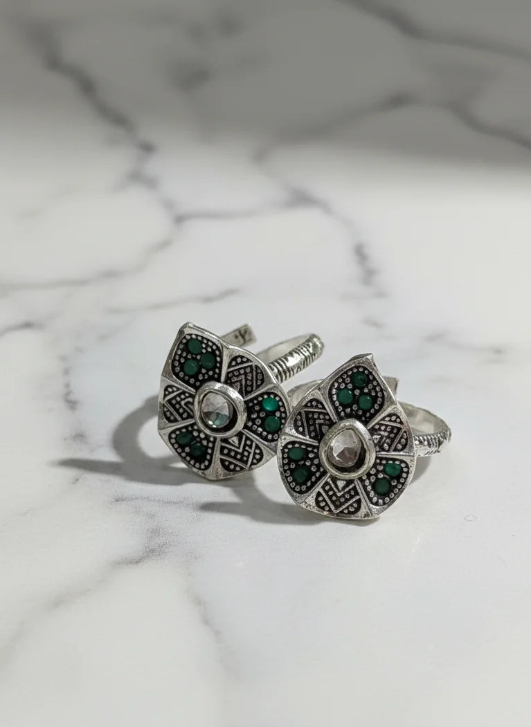 Pair of silver floral toe rings with green gemstones on a marble background