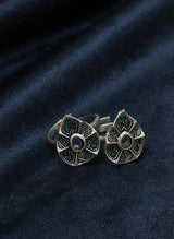 Pair of silver toe rings with green gemstones on a dark blue fabric background