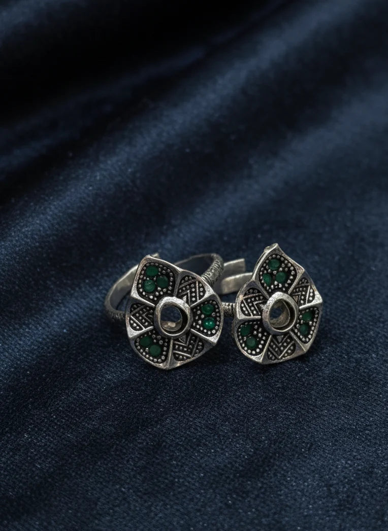 Pair of silver toe rings with green gemstones on a dark blue fabric background