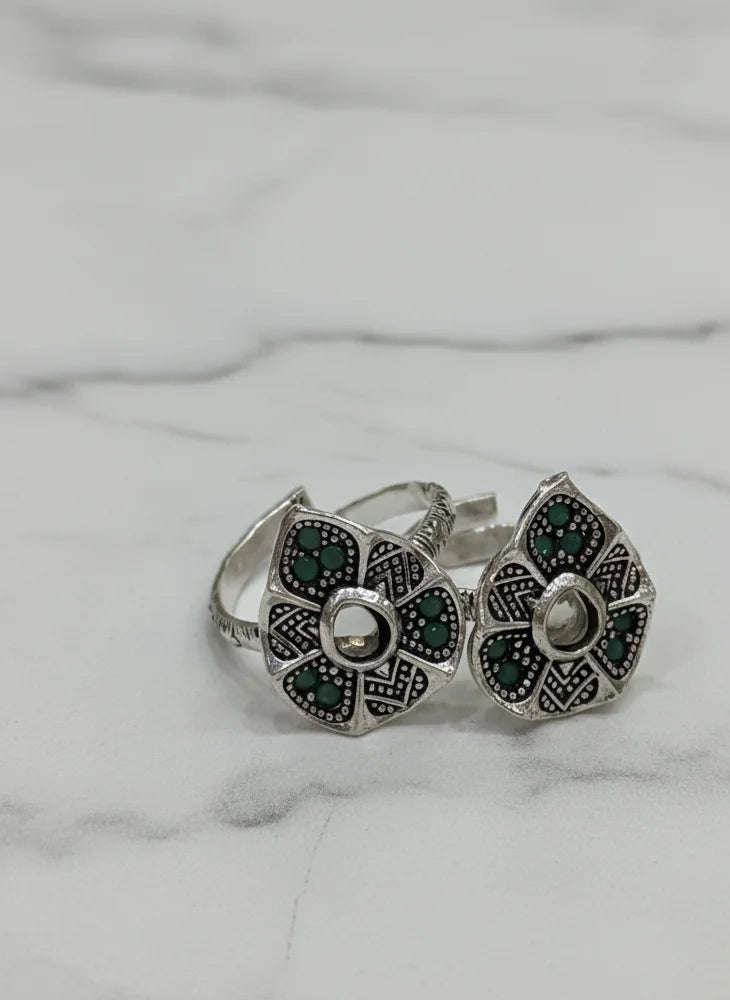 Pair of silver toe rings with green gemstones on a marble surface