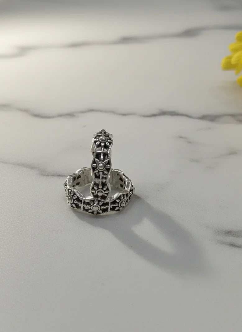 Silver toe ring with intricate design on a marble surface with a yellow flower.