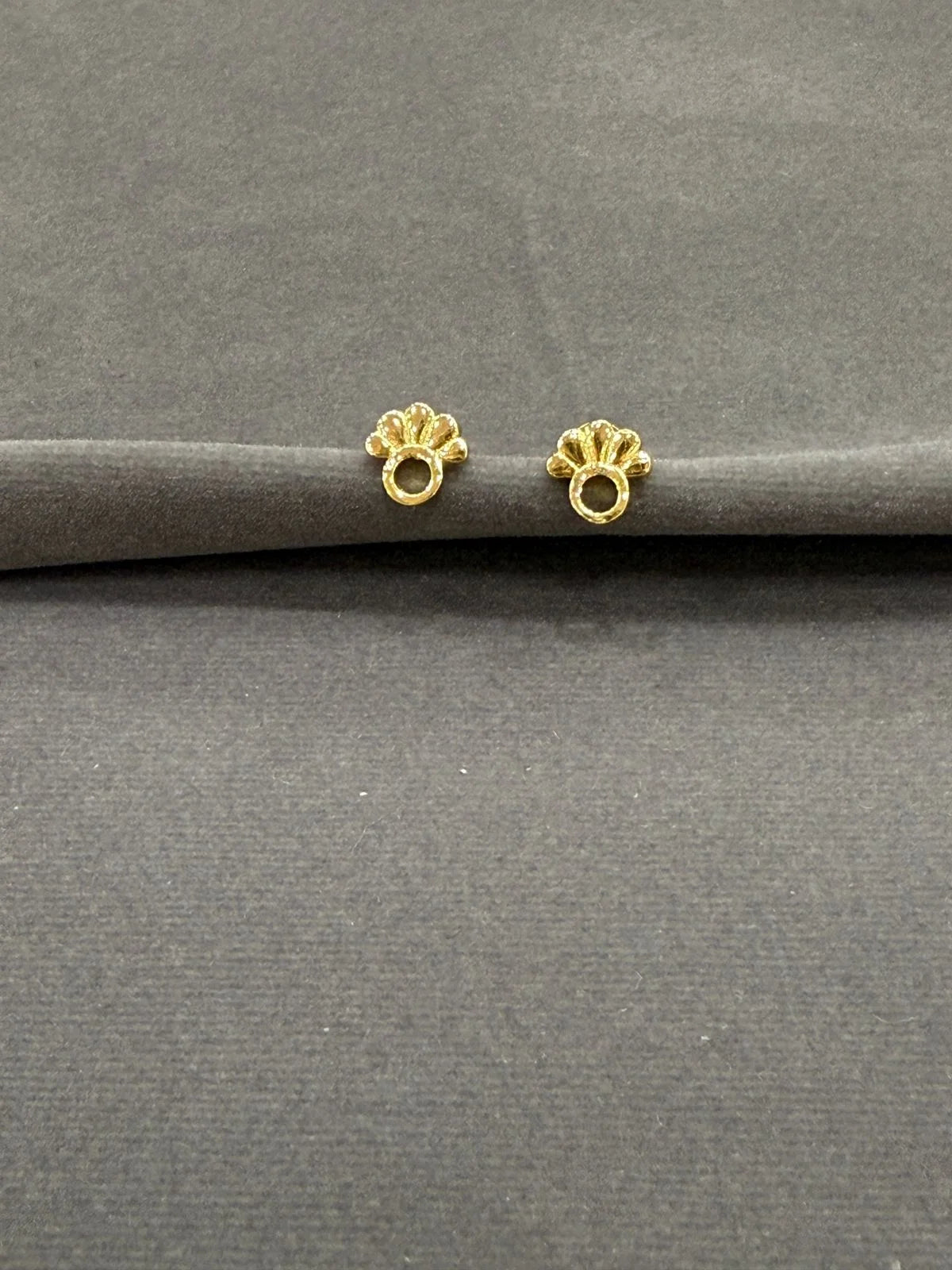 Two gold earrings on a gray surface